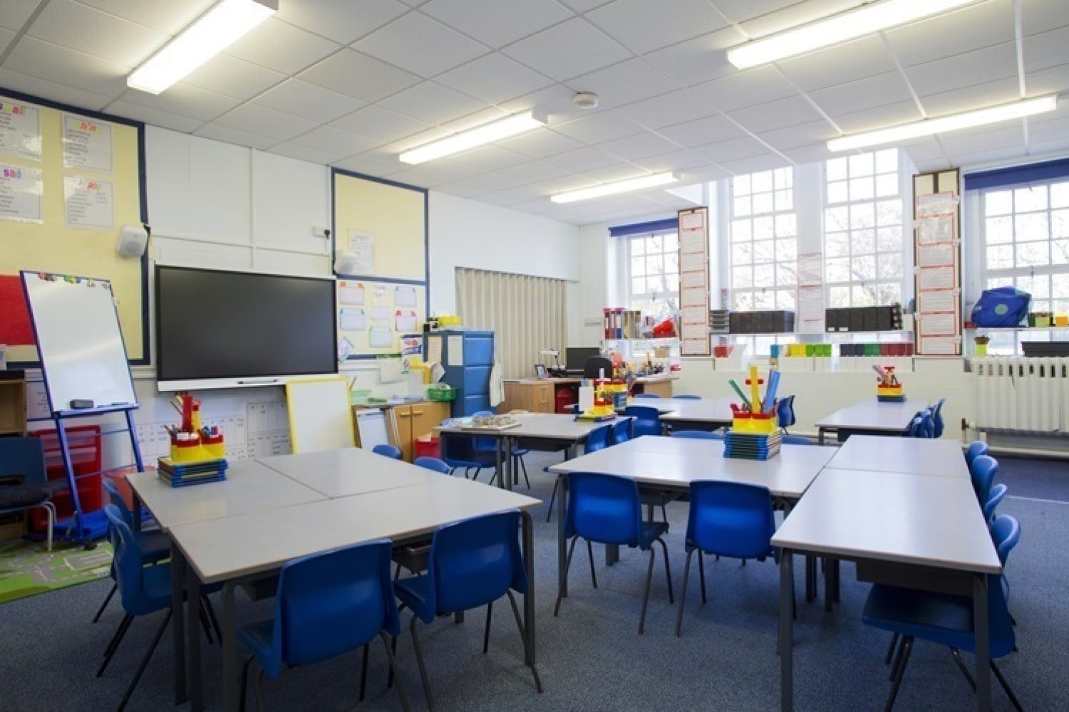 A horizontal image of an empty primary school classroom. The setting is typically British.
