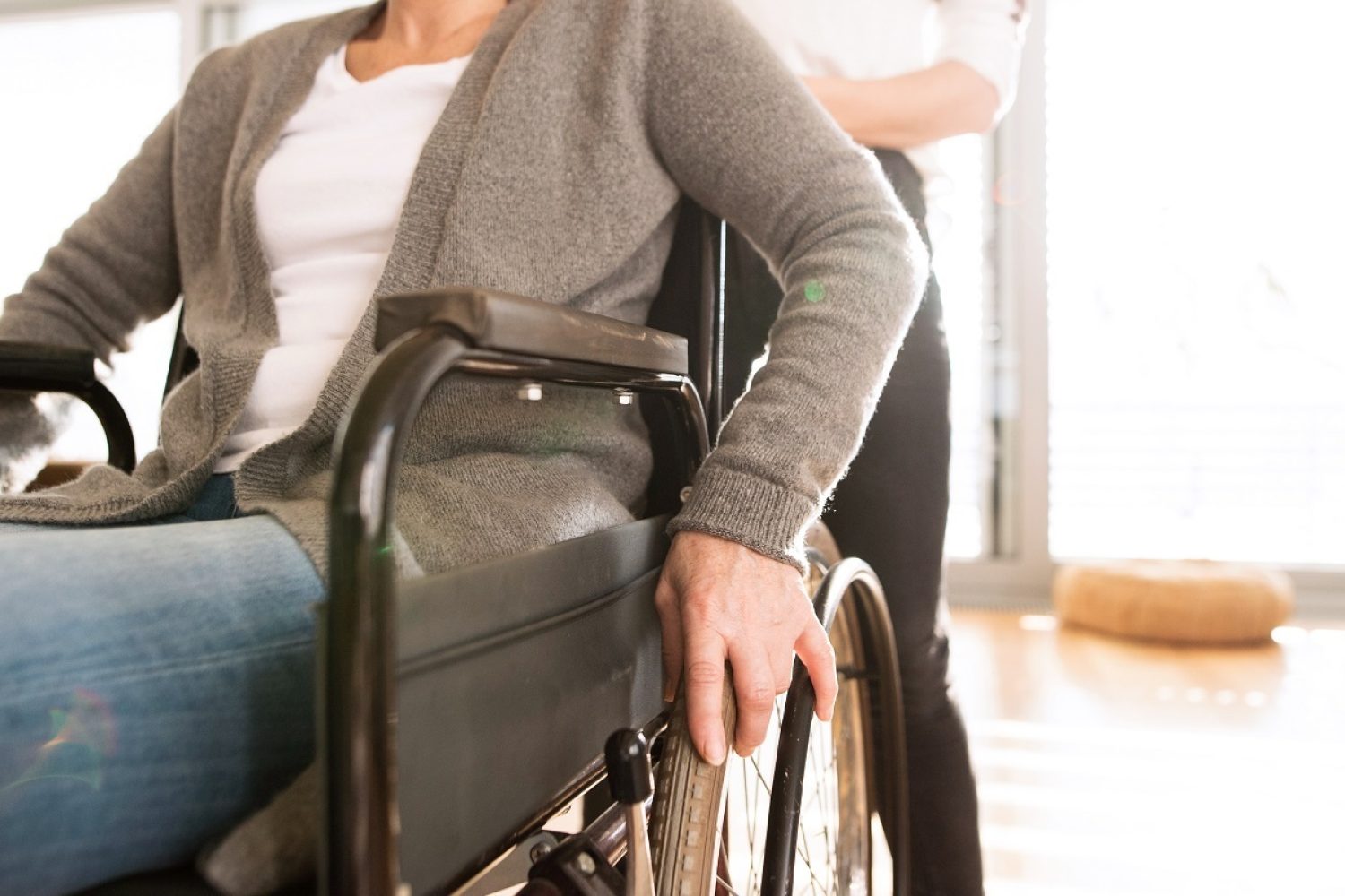 Disabled senior woman in wheelchair at home in her living room, with her young daughter caring for her.