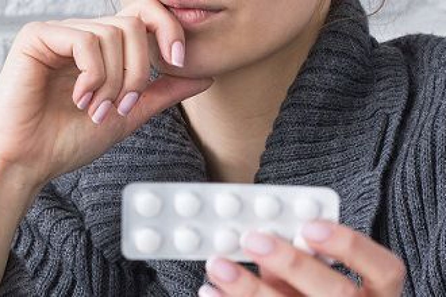 Pretty young woman holding medicine for headache. Sitting sick at home